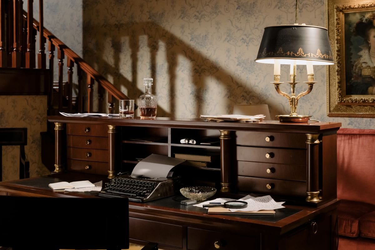 A lamplit writing desk with a typewriter at the foot of a staircase