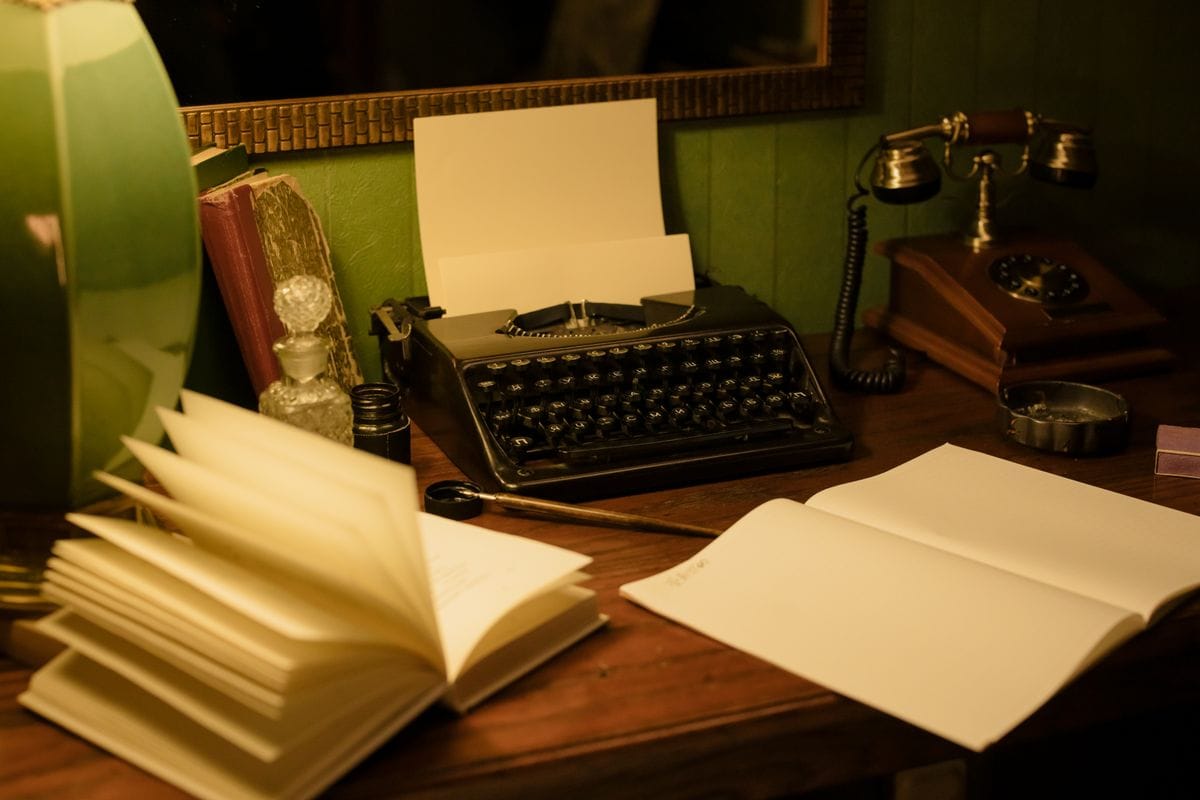 A typewriter and blank pages under warm light in a green study